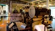 Une vieille presse à imprimer, dotée d’engrenages et de rouleaux de grande taille, entourée de meubles en bois et de pièces métalliques.