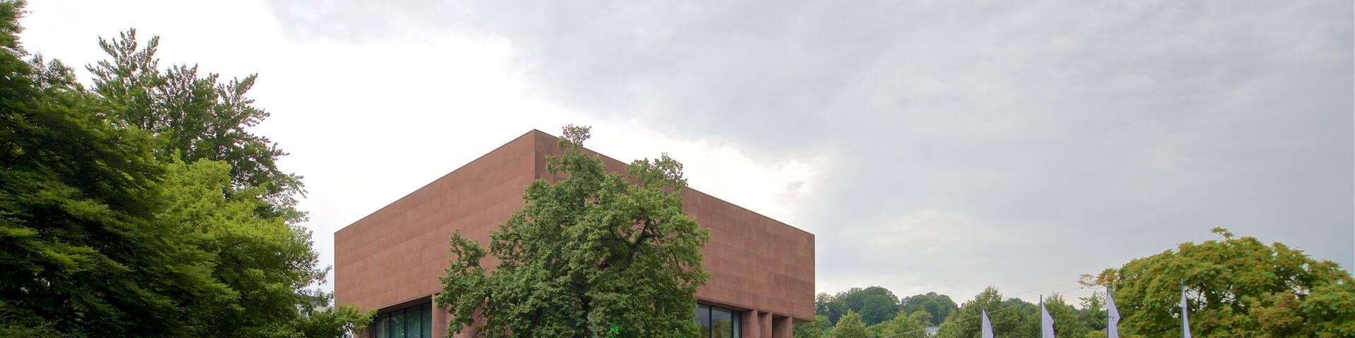 Un edificio moderno con fachada de vidrio, rodeado de un césped cuidado y árboles.
