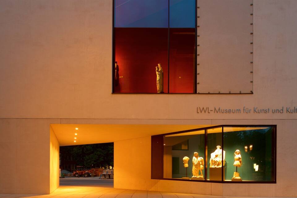 A modern building with a glass facade displaying sculptures.