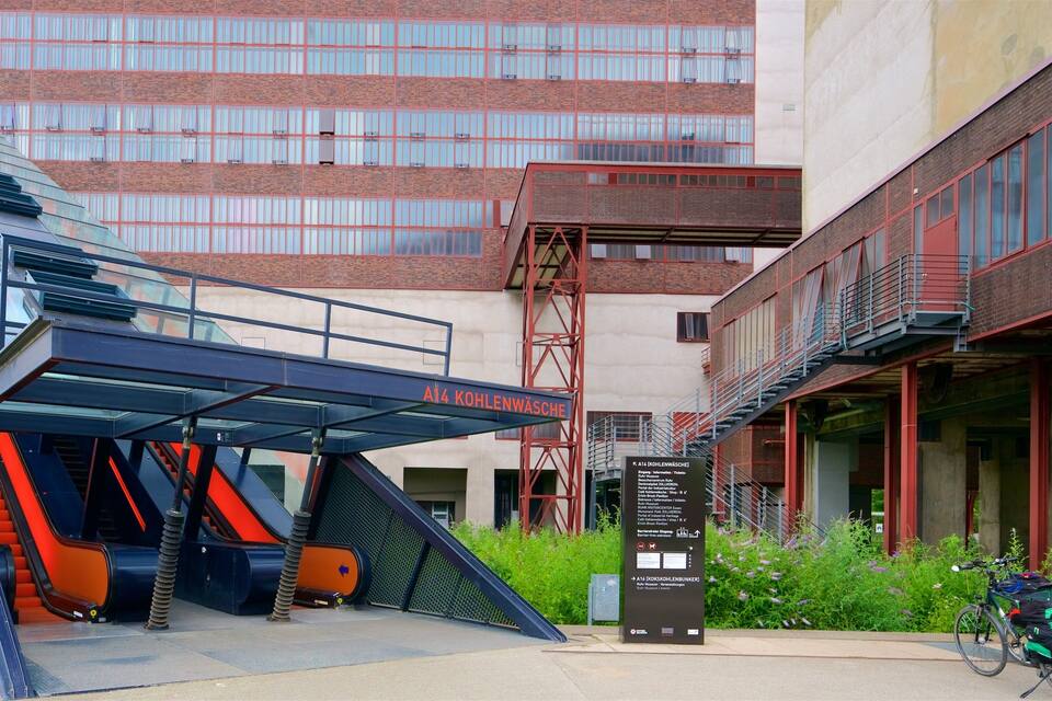 Un edificio moderno con fachada de vidrio y una estructura de ladrillo rojo al fondo.