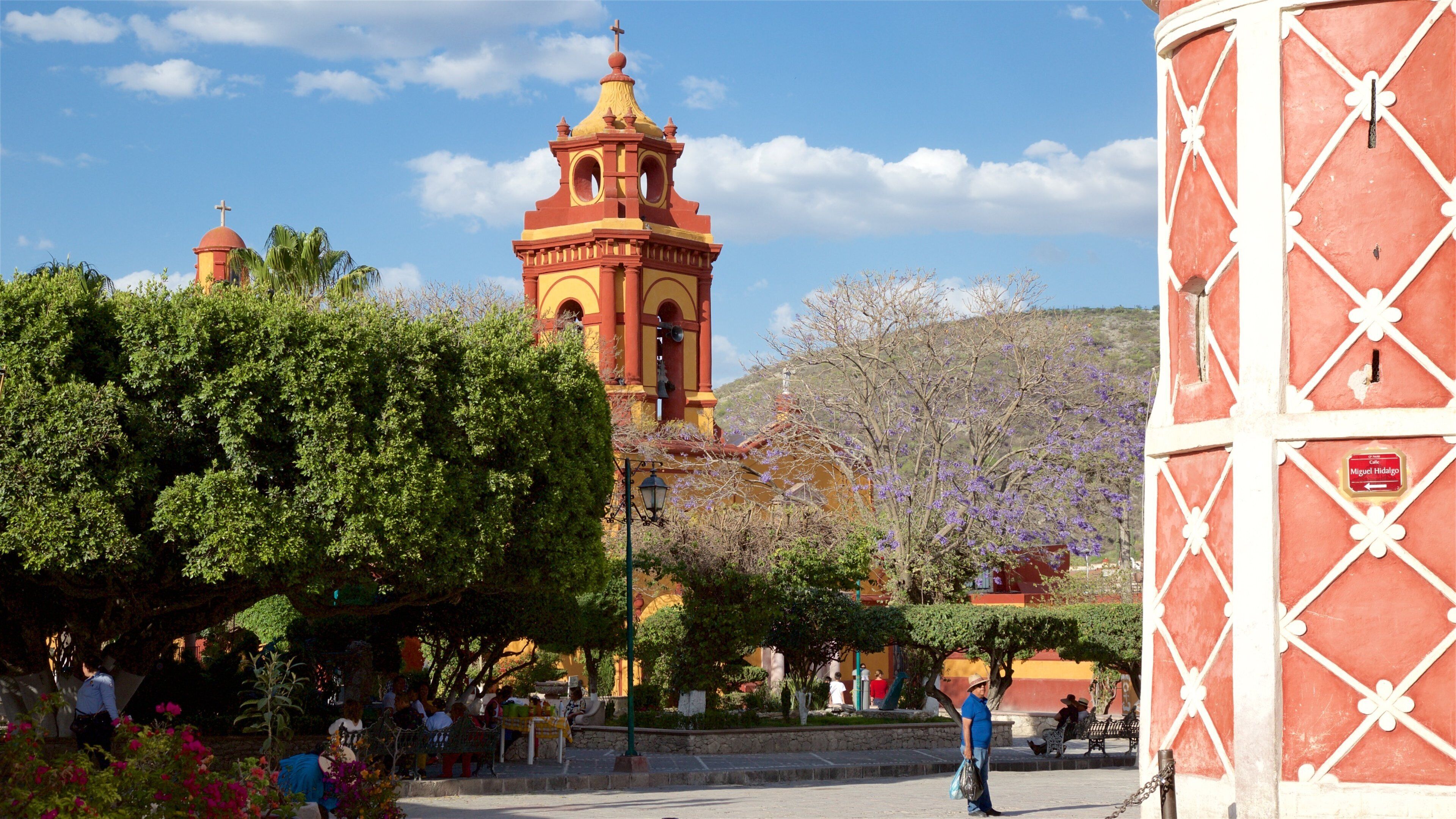 A historic church with a bell tower, surrounded by lush greenery and a clear blue sky.