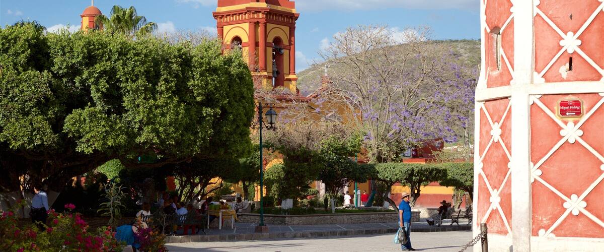 A historic church with a bell tower, surrounded by lush greenery and a clear blue sky.