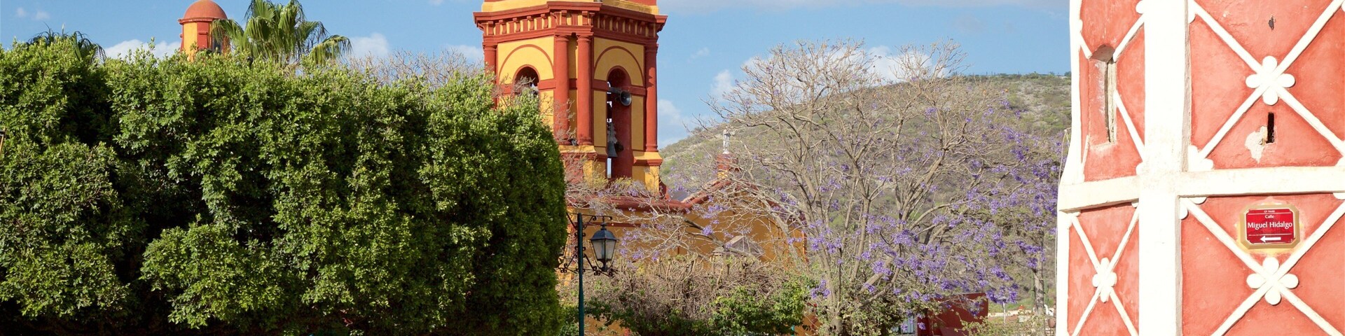 A historic church with a bell tower, surrounded by lush greenery and a clear blue sky.