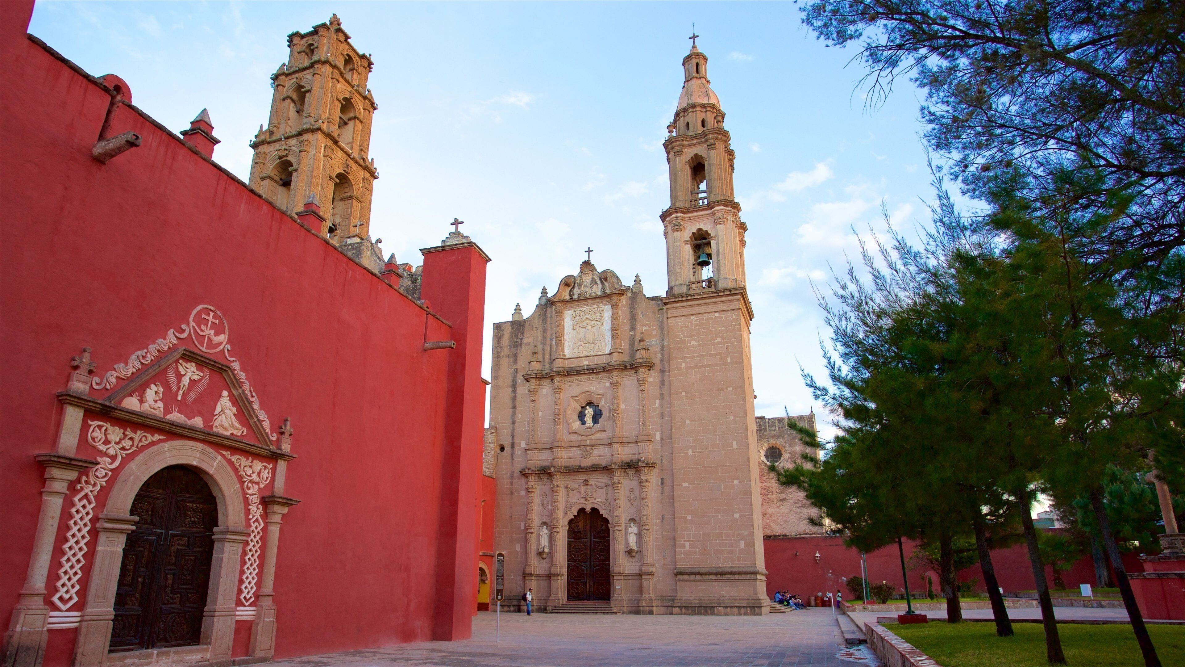 A historic church with two bell towers and a red wall with ornate carvings.