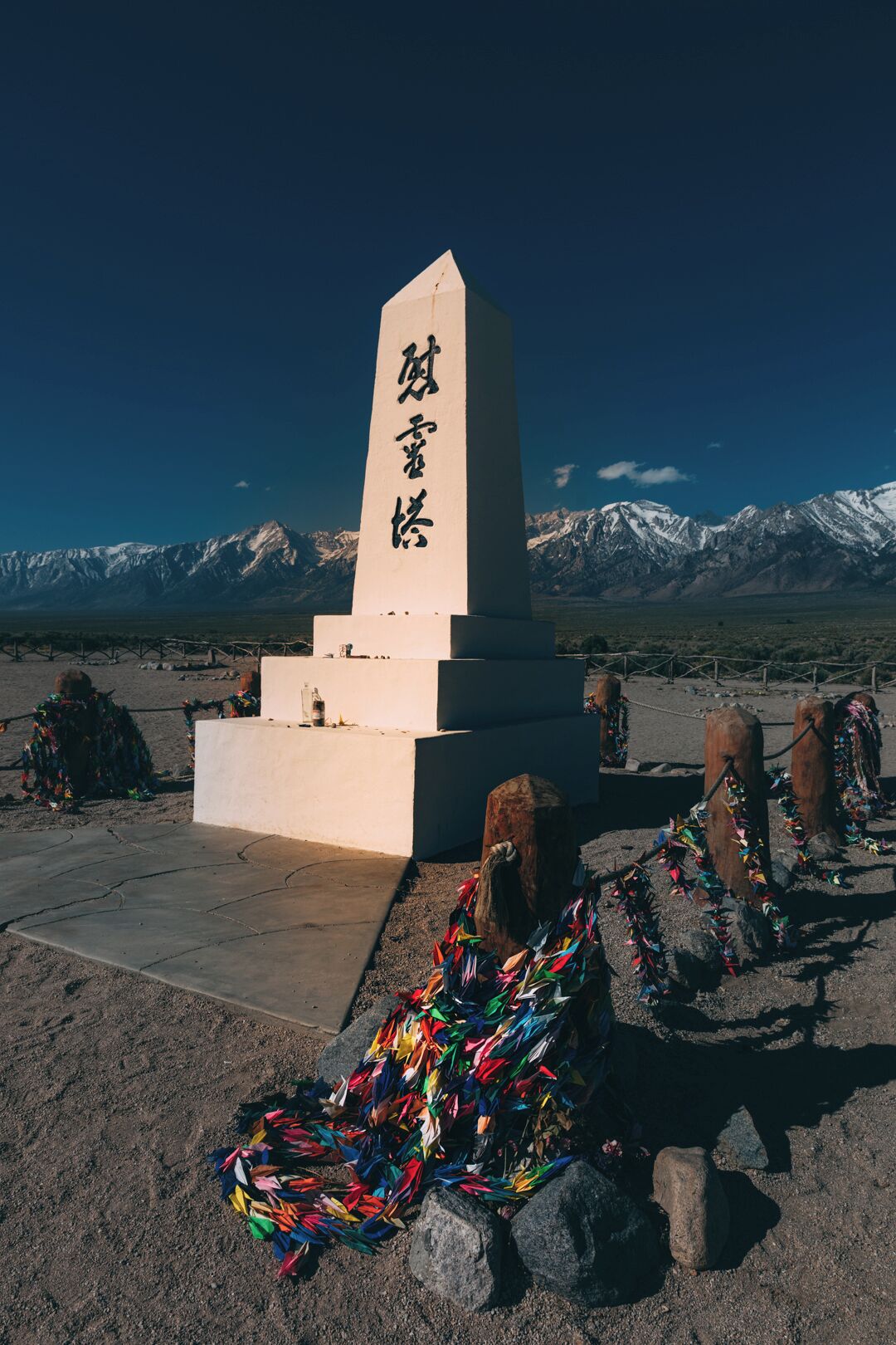 A monument with inscriptions, surrounded by colorful prayer flags and a mountainous backdrop.