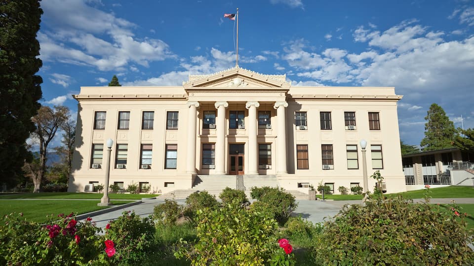 A stately building with a flagpole, columns, and a well-maintained garden.