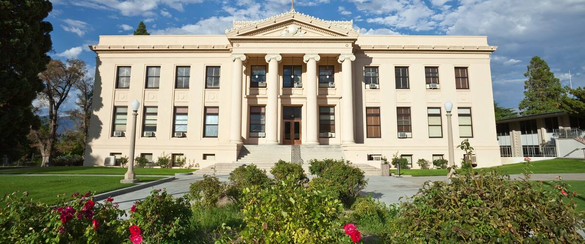 A stately building with a flagpole, columns, and a well-maintained garden.