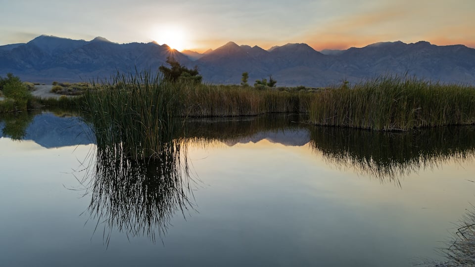 A mountain range at sunrise with a calm lake reflecting the scenery.