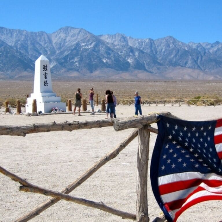 A desert landscape with a wooden fence, an American flag, and a white monument with Chinese characters.