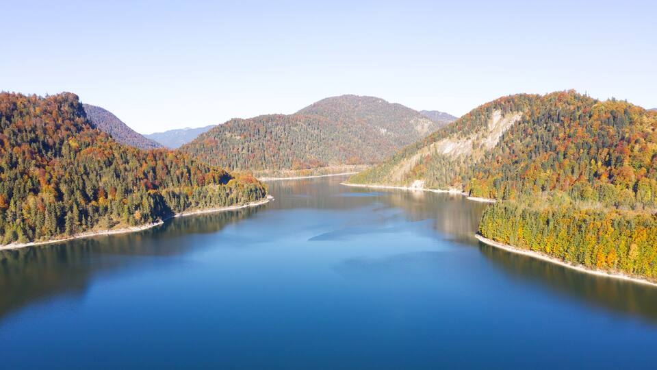 A calm lake surrounded by forested hills with autumn foliage.