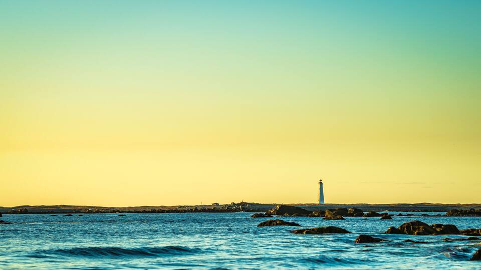 A lighthouse on a rocky shoreline at sunset.