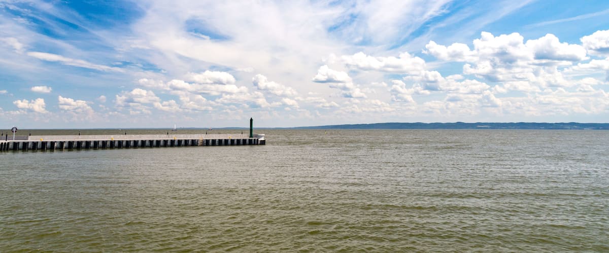 A pier extending into calm waters under a partly cloudy sky.