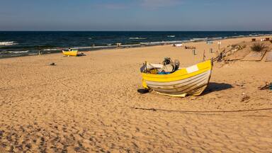A sandy beach with a yellow boat and a few people in the distance.