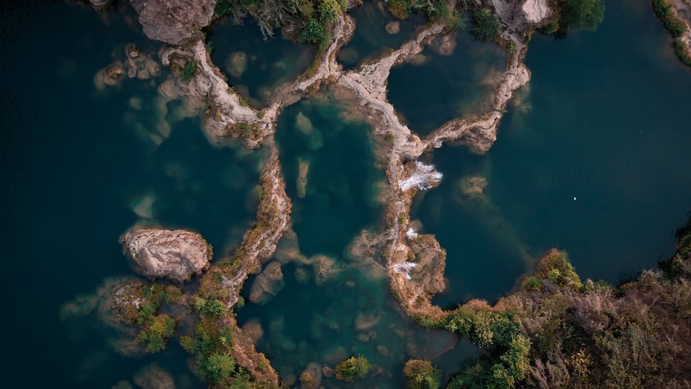 Ein Fluss mit klarem Wasser, umgeben von felsigem Gelände und spärlicher Vegetation.