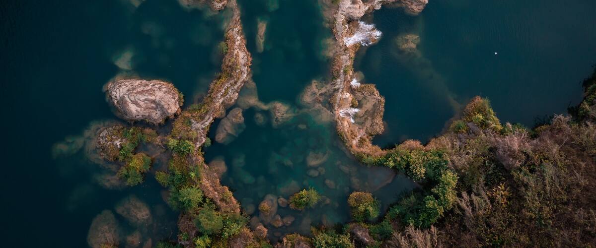 A river with clear water, surrounded by rocky terrain and sparse vegetation.