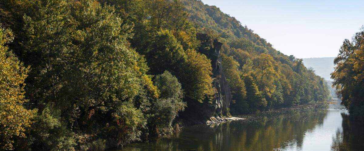 The autumn landscape with the “Cockerel” rock is reflected in the mountain river Psekups. Sunny day in the resort area of Goryachiy Klyuch. Krasnodar region.