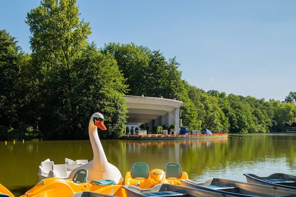 Eine Schwanstatue, gelbe Boote und ein überdachtes Gebäude am Seeufer.