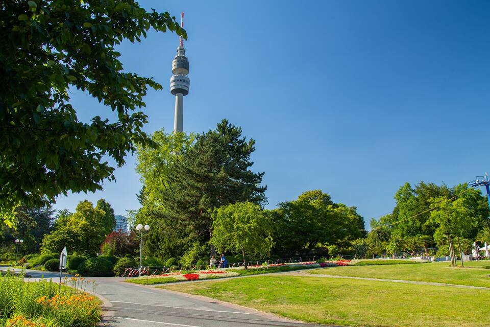 Um parque com uma torre, árvores e um céu claro.