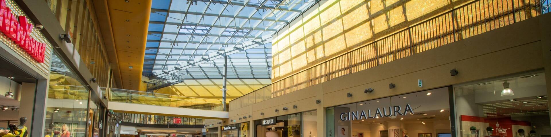 Un centro comercial moderno con techo de cristal, varios niveles y diversas tiendas.
