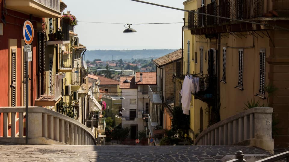 A cobblestone street with buildings on either side, a no parking sign, and a view of the countryside in the distance.
