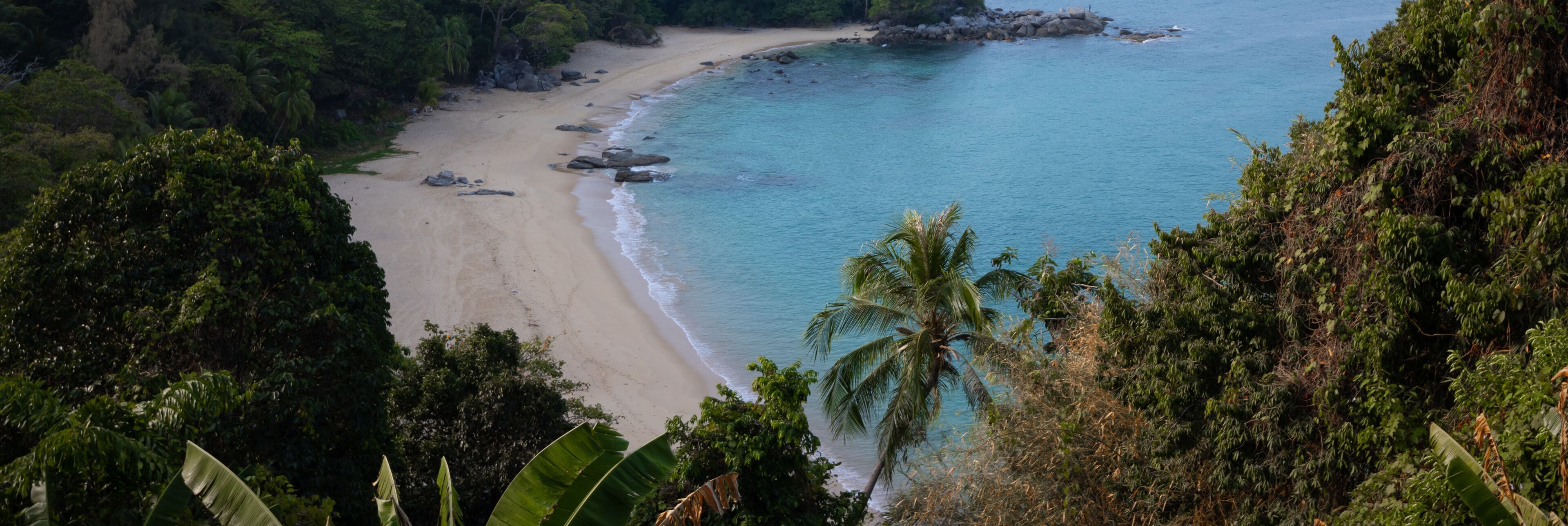 A tropical beach with clear turquoise waters, sandy shore, and lush greenery.