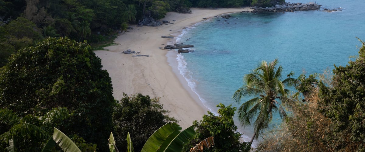 A tropical beach with clear turquoise waters, sandy shore, and lush greenery.