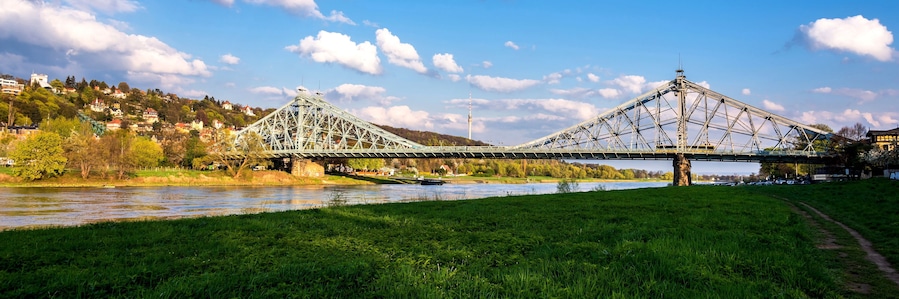 Eine große Stahlbrücke überspannt einen Fluss, im Hintergrund ist eine Stadtlandschaft zu sehen.