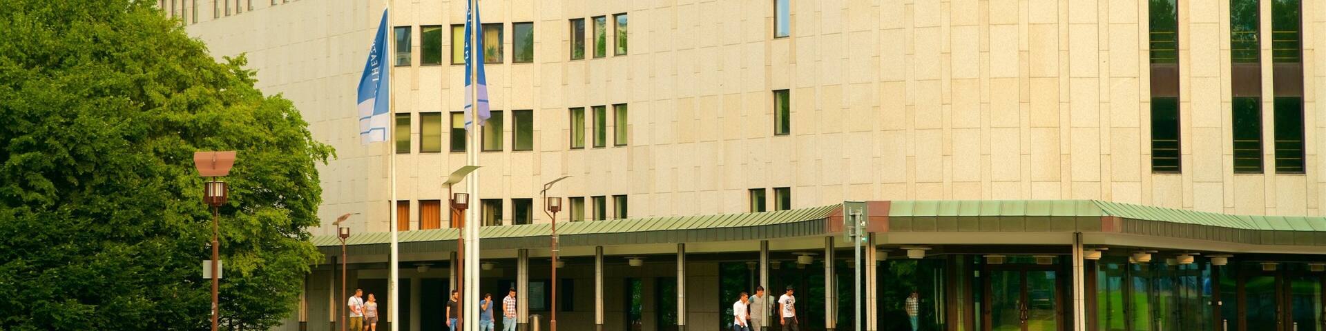 A modern building with a curved facade, multiple windows, and a covered entrance area.
