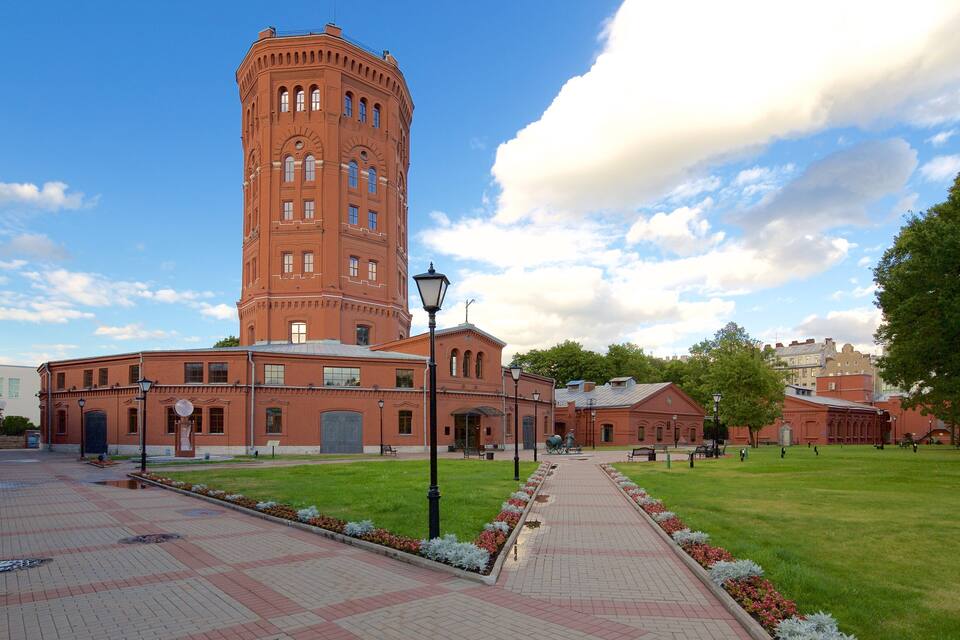 Ein historisches Gebäude aus rotem Backstein mit einem Turm, einem gepflasterten Weg und einer Rasenfläche.