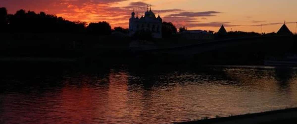 A sunset over a river with a castle silhouette and a bridge.