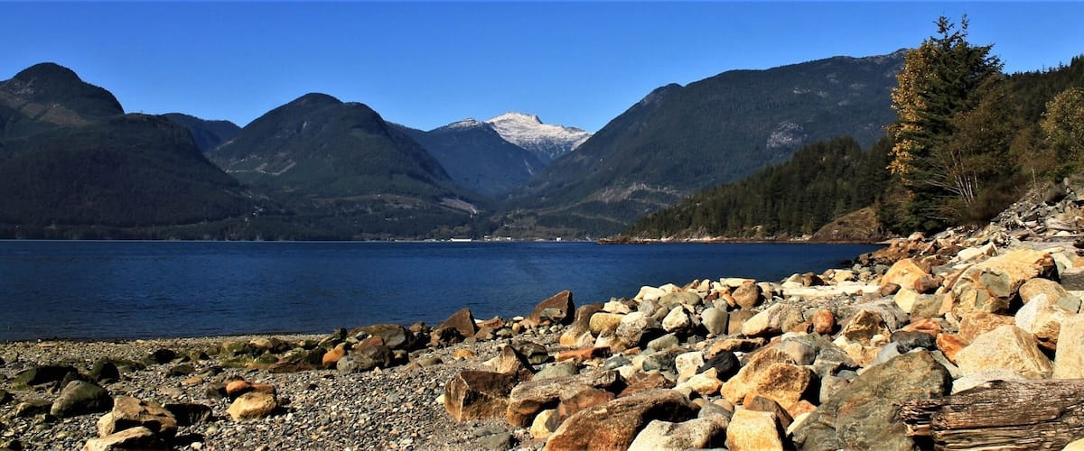 A rocky shoreline with a clear lake and mountains in the background.