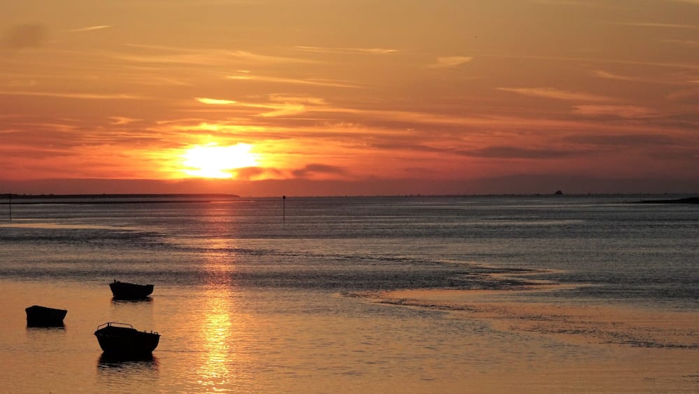A sunset over a calm sea with boats on the shore.