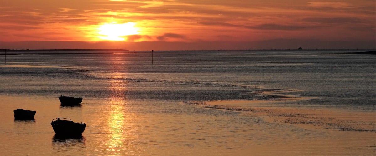 A sunset over a calm sea with boats on the shore.