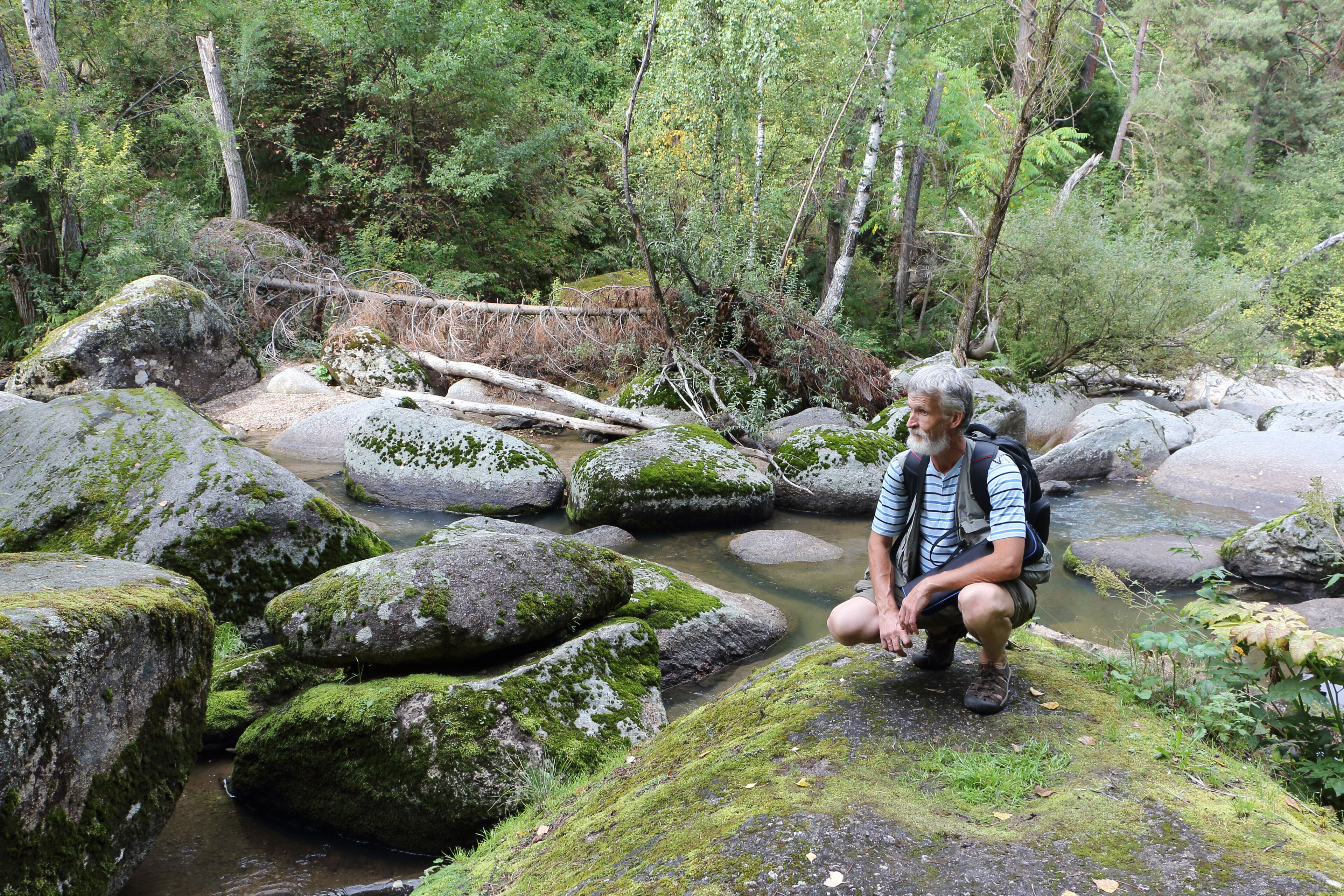 Man with a backpack sitting on a stone near a mountain river on a summer day, Belokurikha River, Altai Mountains
