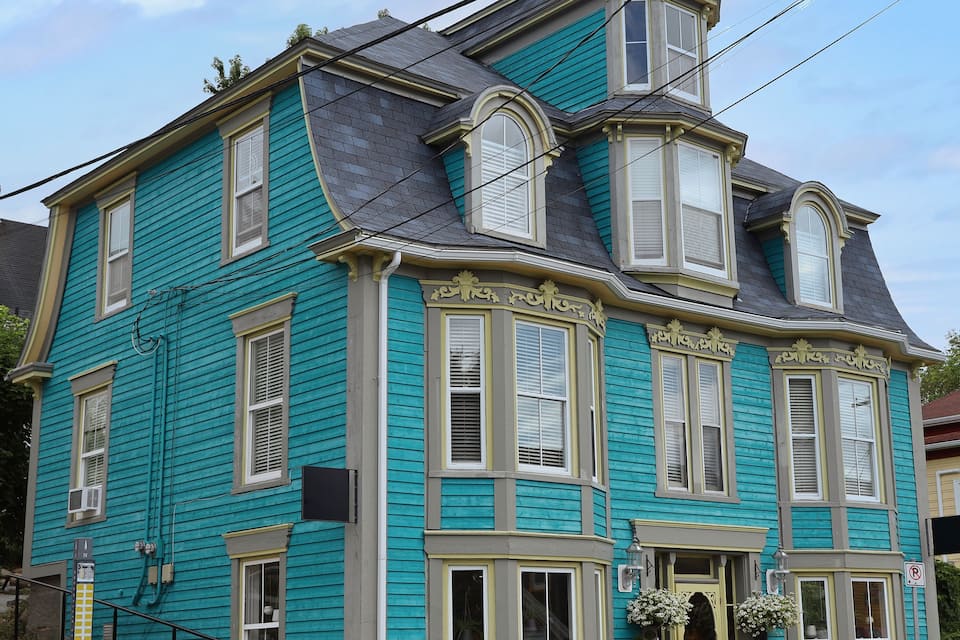 A turquoise Victorian-style house with a bay window, a front porch with flower baskets, and a 'No Parking' sign.
