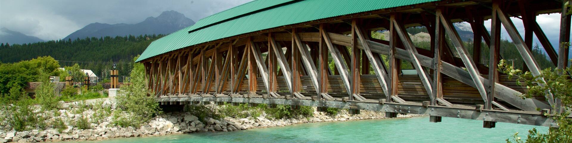 A wooden bridge over a turquoise river with mountains in the background.