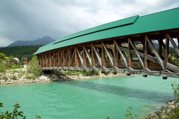 Un pont en bois enjambe une rivière aux eaux turquoise, avec des montagnes en arrière-plan.