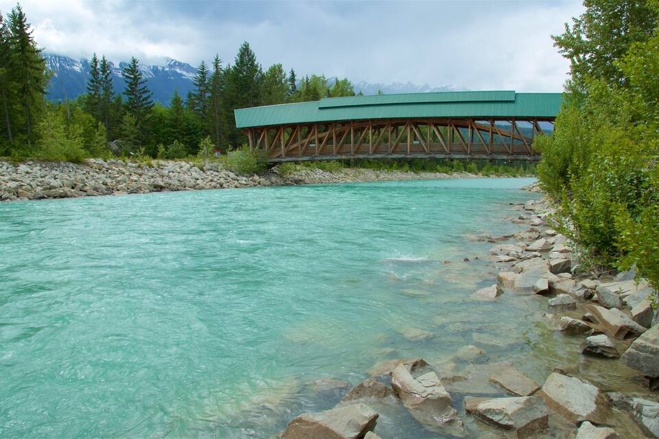 Um rio azul-turquesa com águas cristalinas, rodeado por rochas e vegetação, e uma ponte de madeira ao fundo.
