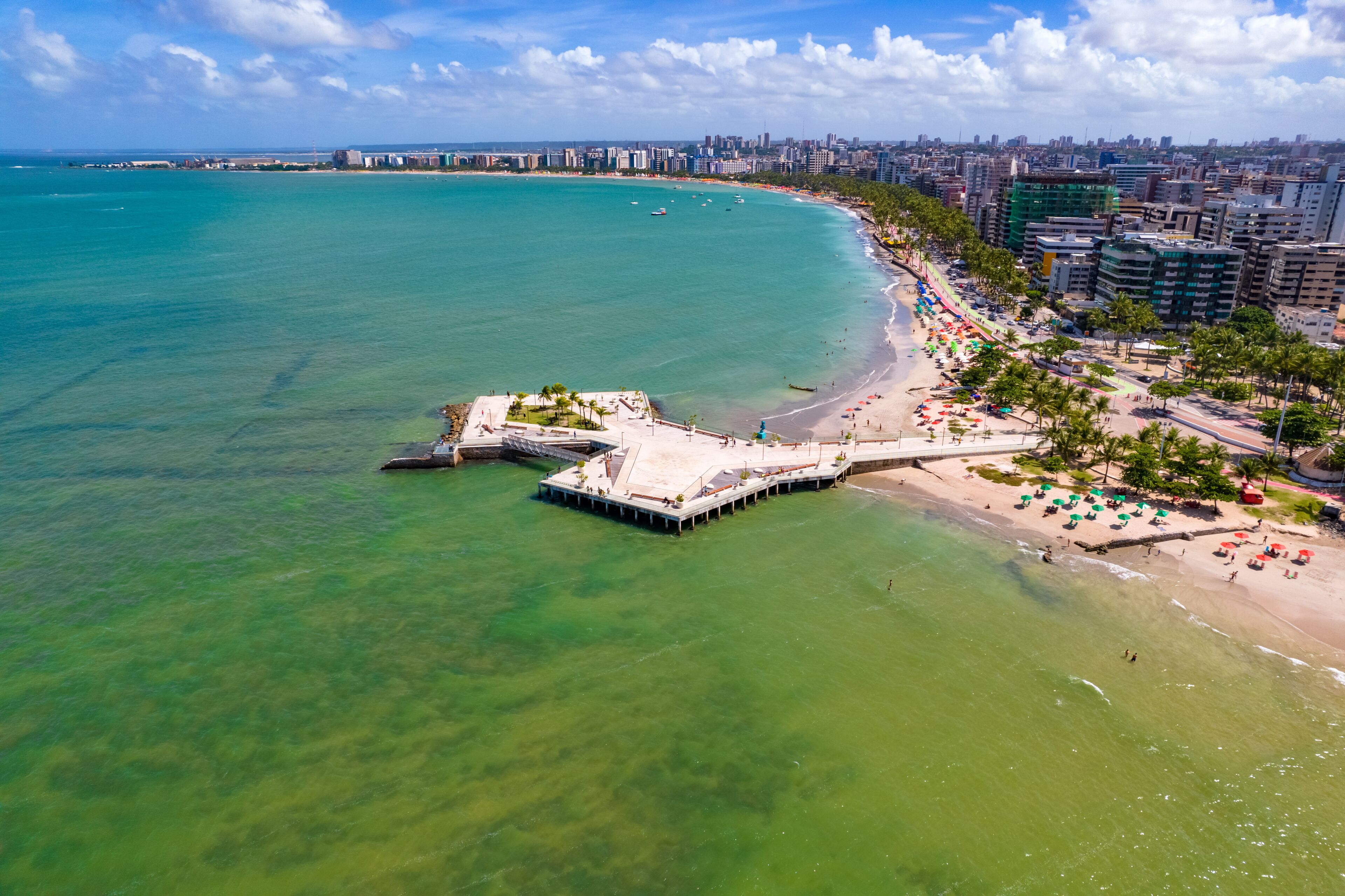 Paisagem costeira com praia, um píer e edifícios altos.
