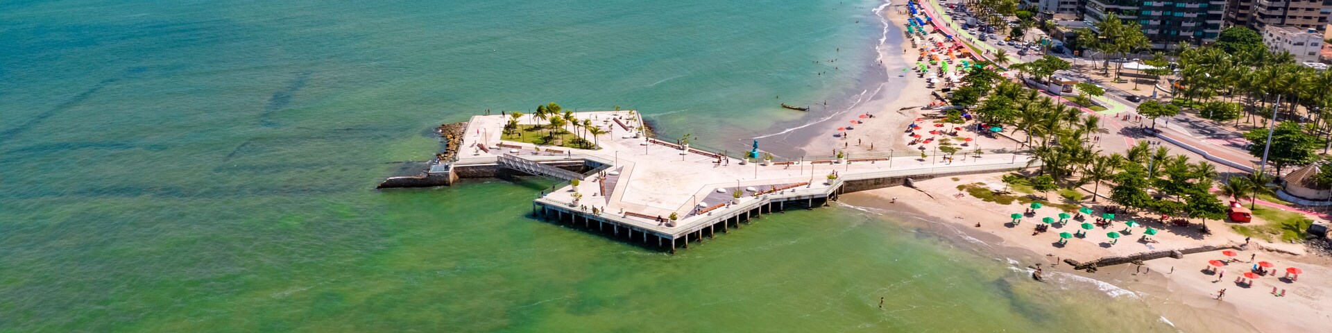 Paisagem costeira com praia, um píer e edifícios altos.