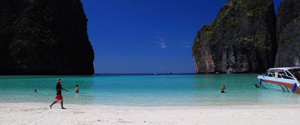 A beach with clear turquoise water, a boat named 'Myrinda Tour', and large limestone cliffs.