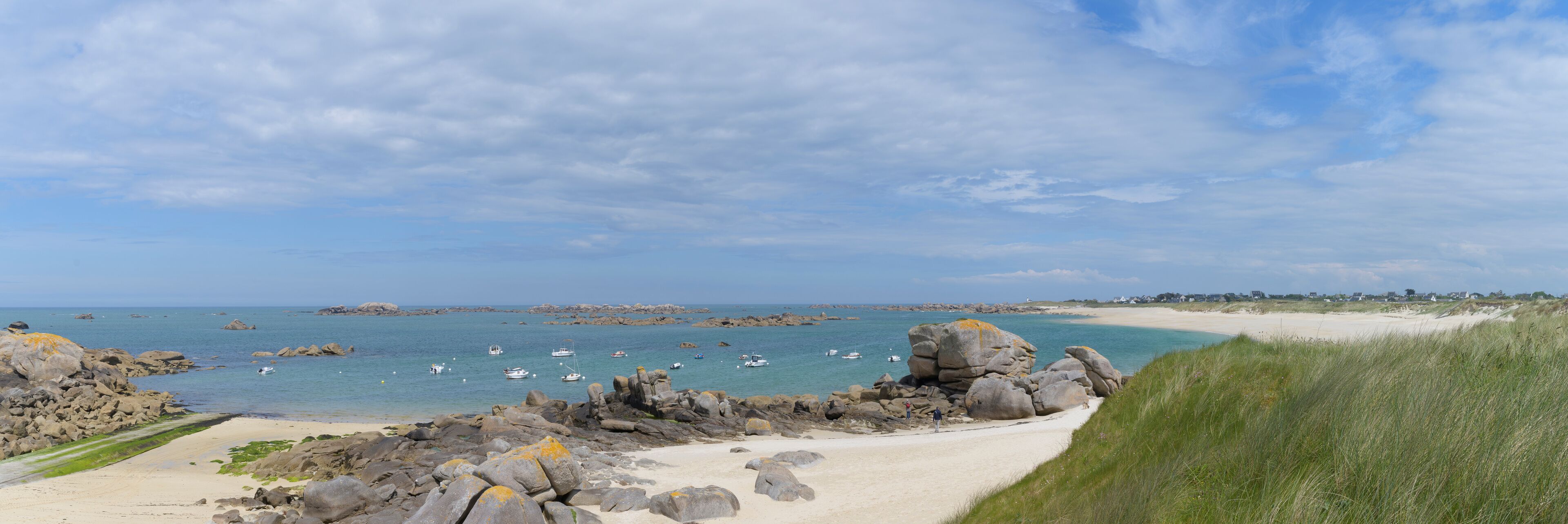 A coastal landscape with a sandy beach, rocky outcrops, and calm sea with boats.