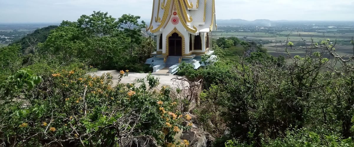 A white temple with golden accents surrounded by lush greenery and a distant landscape.