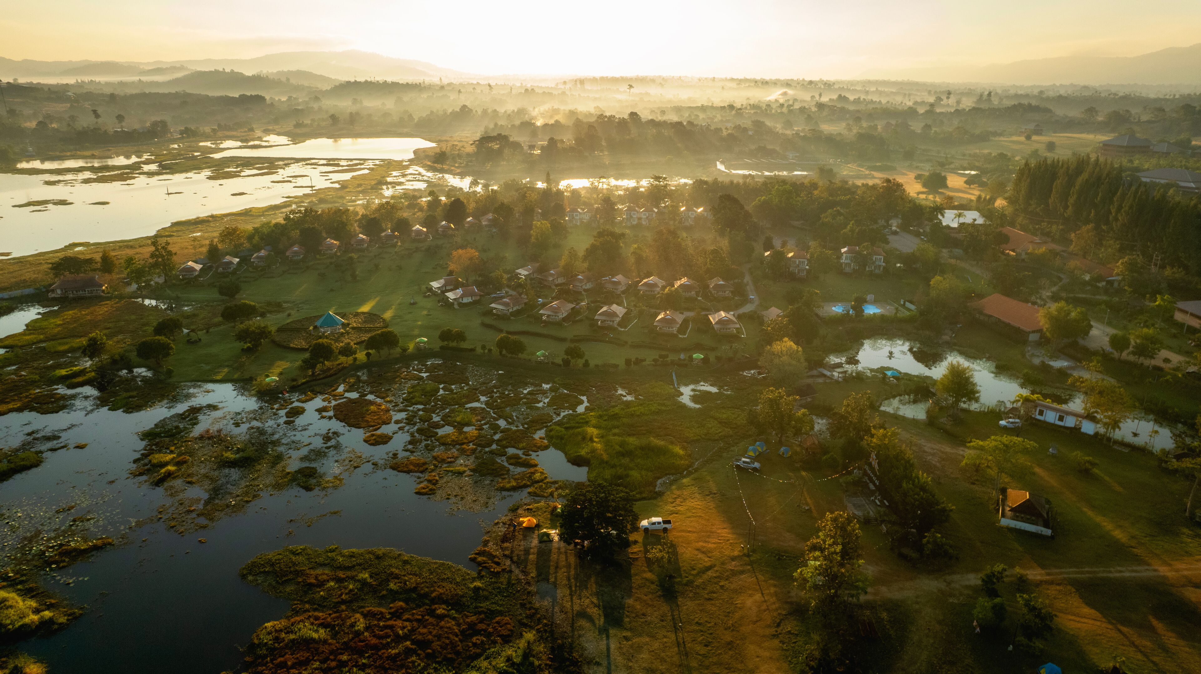 A rural landscape with a lake, houses, and surrounding greenery.