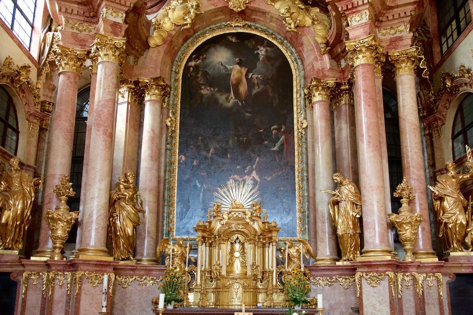 L’intérieur d’une église richement décorée, avec des statues dorées, des colonnes de marbre et une grande fresque murale.