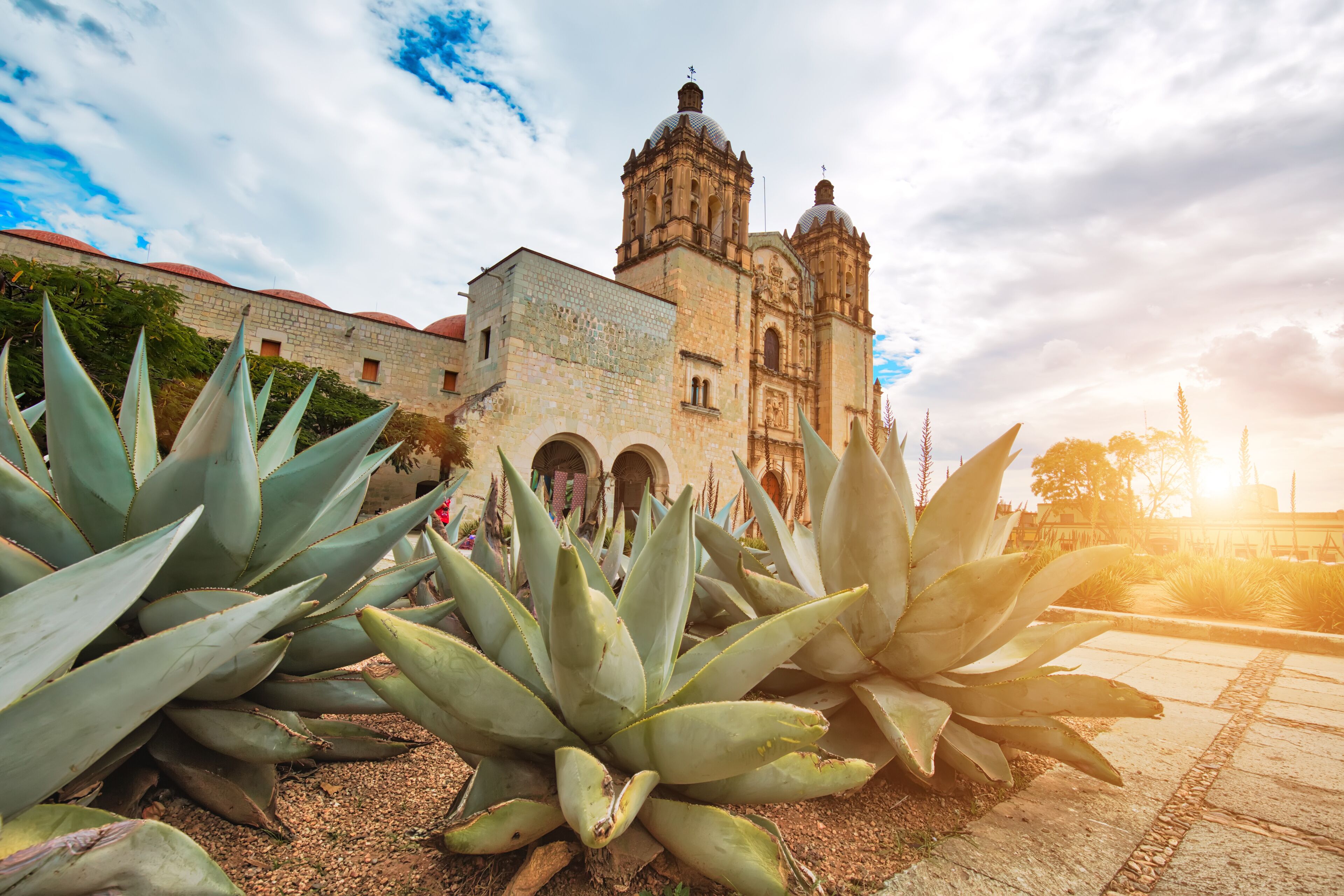 A historic building with domed towers and arches, surrounded by agave plants.