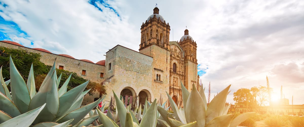 A historic building with domed towers and arches, surrounded by agave plants.