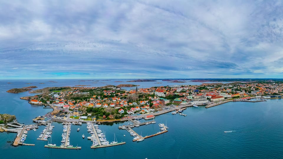 An aerial view of a coastal town with a marina, colorful houses, and a lighthouse.