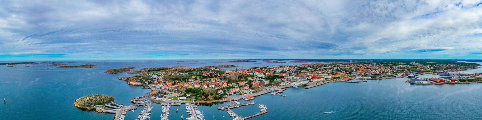 An aerial view of a coastal town with a marina, colorful houses, and a lighthouse.