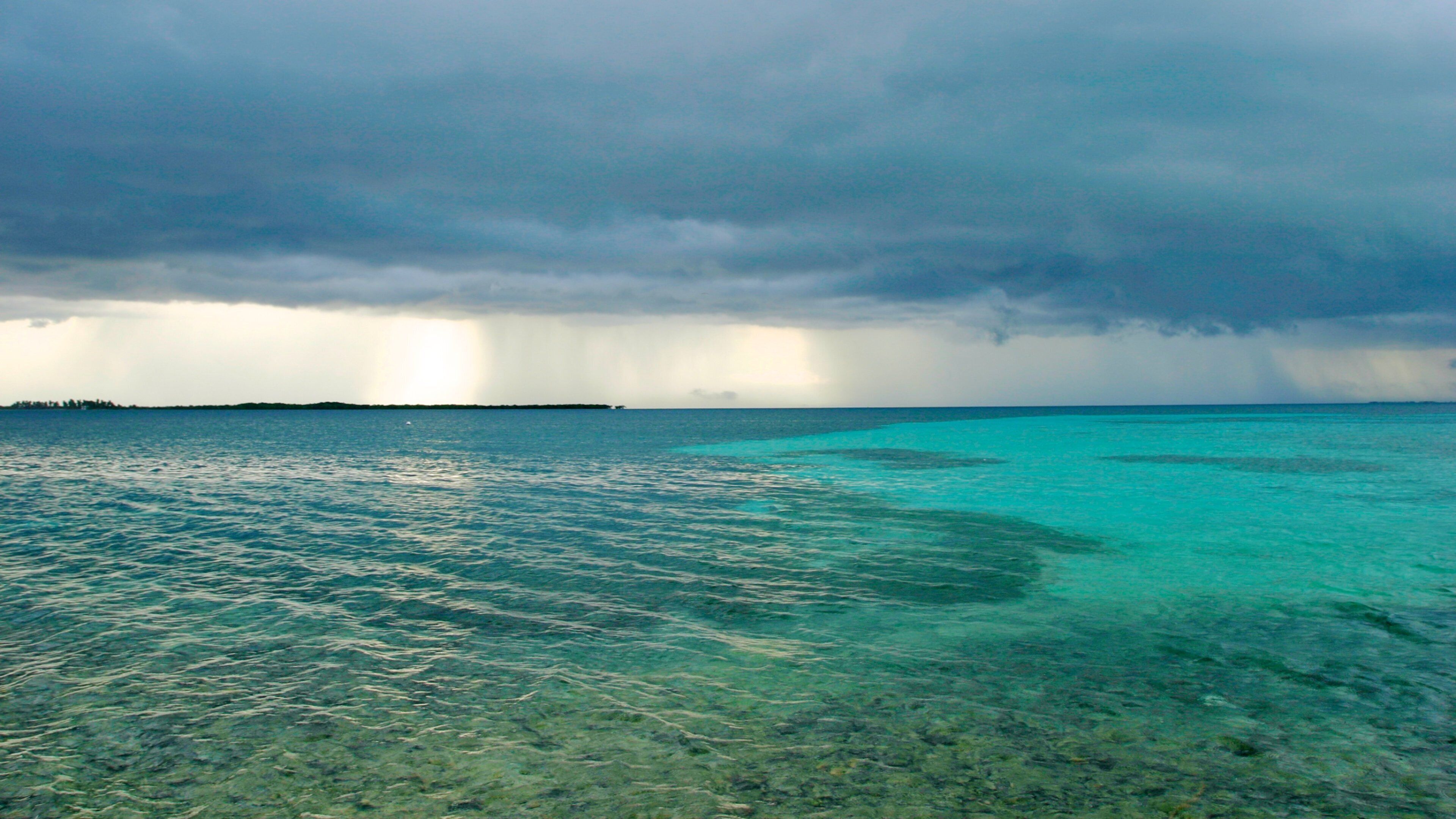 A turquoise sea with clear shallow waters and a distant landmass under a cloudy sky.